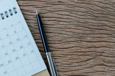 White clean calendar with pen on wooden table background with copy space, business meeting schedule, travel planning or project milestone and reminder concept.